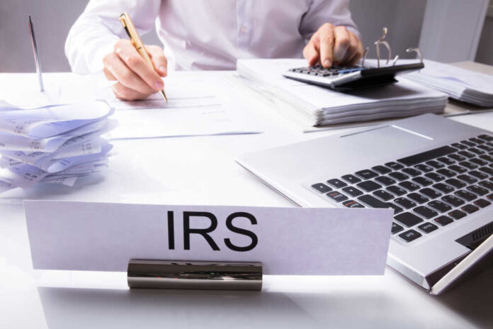 Irs,Nameplate,In,Front,Of,Accountant,Calculating,Tax,On,Desk
