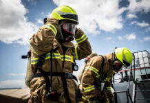 Firefighters in protective gear standing outside cloudy sky