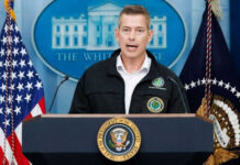 Man speaking at podium with presidential seal and flags