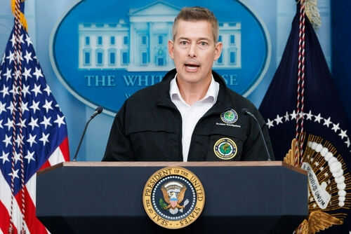 Man speaking at podium with presidential seal and flags