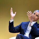 A man in a suit gesturing while speaking at an event