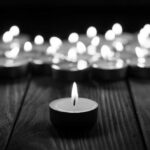 Single candle burning among many on wooden surface.