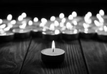 U.S. Betrayal? Afghan Ally Dies in Custody Single candle burning among many on wooden surface.