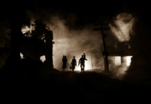 Silhouettes walking through smoky destroyed urban landscape night