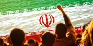 Crowd of people with their hands raised in front of the Iranian flag