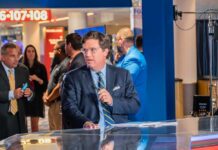 News anchor presenting in a television studio with a crowd in the background