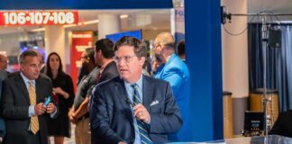 News anchor presenting in a television studio with a crowd in the background