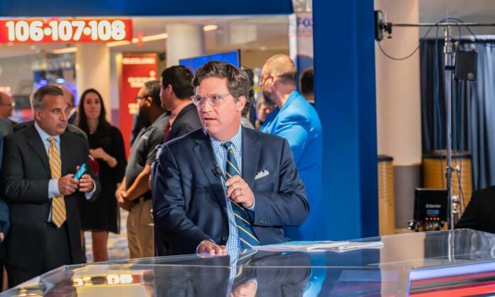 News anchor presenting in a television studio with a crowd in the background