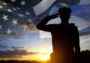 Silhouette of a person saluting against an American flag backdrop during sunset