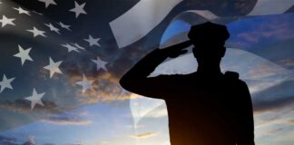 Silhouette of a person saluting against an American flag backdrop during sunset