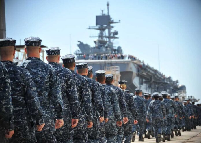 shutterstock_2597859511.jpg Navy personnel marching in formation towards a ship