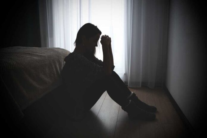 A silhouette of a woman sitting on the floor, looking contemplative near a window