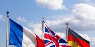 Flags of France, the United Kingdom, and Germany waving against a blue sky