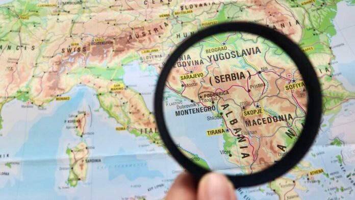 A hand holding a magnifying glass over a map highlighting Serbia and surrounding countries