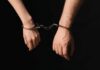 Two hands connected by handcuffs against a dark background