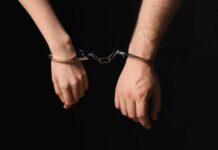 Two hands connected by handcuffs against a dark background