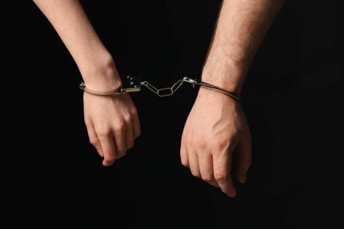shutterstock_2695049117.jpg Two hands connected by handcuffs against a dark background