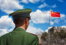 Soldier in a green military uniform facing the Great Wall of China with the Chinese flag in the background