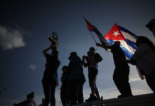 Silhouetted figures holding a trophy and Cuban flags during a celebration