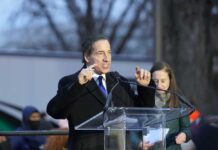 A man speaking passionately at a podium during an outdoor event