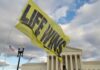 A large yellow flag with the words 'LIFE WINS' waving in front of the Supreme Court building