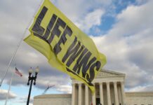 A large yellow flag with the words 'LIFE WINS' waving in front of the Supreme Court building