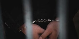 Close-up of handcuffed hands behind bars