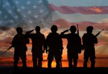Silhouetted soldiers saluting against an American flag backdrop at sunset