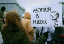 Person holding a sign that reads 'Abortion is Murder' at a protest