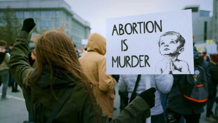 Person holding a sign that reads 'Abortion is Murder' at a protest