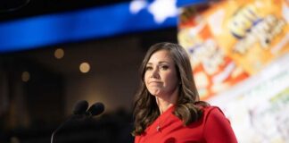 A woman in a red dress speaking at a podium with microphones
