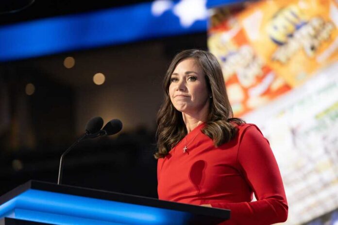 A woman in a red dress speaking at a podium with microphones