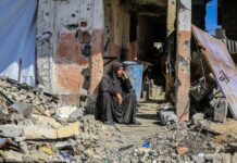 A woman sitting among rubble outside a damaged building