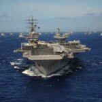 An aircraft carrier surrounded by various naval vessels in the ocean