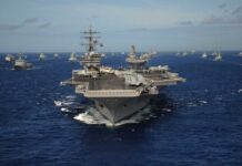 Trump’s Naval Stranglehold—Economic Warfare Unleashed An aircraft carrier surrounded by various naval vessels in the ocean