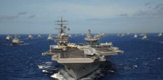 An aircraft carrier surrounded by various naval vessels in the ocean