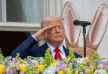 A man in a suit saluting in front of a floral display during an Easter event