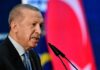 Middle East on Edge: Turkey’s Invasion Warning A political leader speaking into a microphone with a national flag in the background