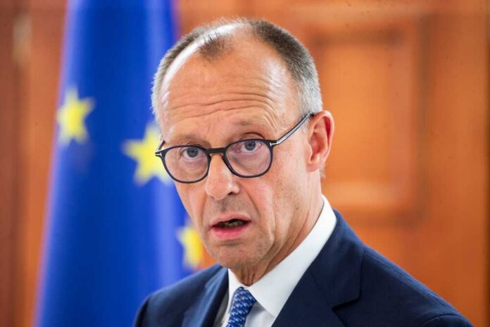 A man in a suit with glasses, looking serious in front of an EU flag