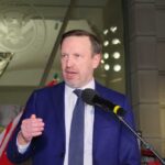 Murphy’s International Move: Escalating U.S. Political War A man in a blue suit speaking at a protest with signs in the background