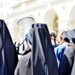 Group of nuns in black attire gathered outdoors, one holding a megaphone
