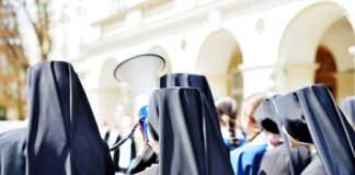 Group of nuns in black attire gathered outdoors, one holding a megaphone
