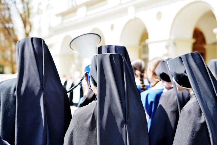 Group of nuns in black attire gathered outdoors, one holding a megaphone