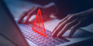 Hands typing on laptop with warning symbol