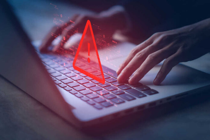 Hands typing on laptop with warning symbol