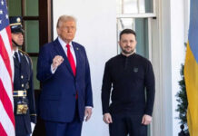 Two men standing near flags and a guard