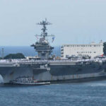 Aircraft carrier with sailors on deck at harbor.