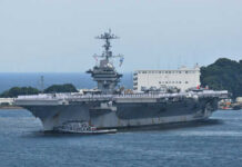 Aircraft carrier with sailors on deck at harbor.