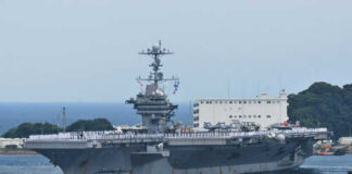 Aircraft carrier with sailors on deck at harbor.