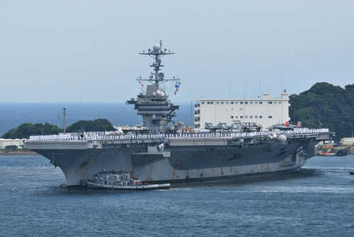 Aircraft carrier with sailors on deck at harbor.